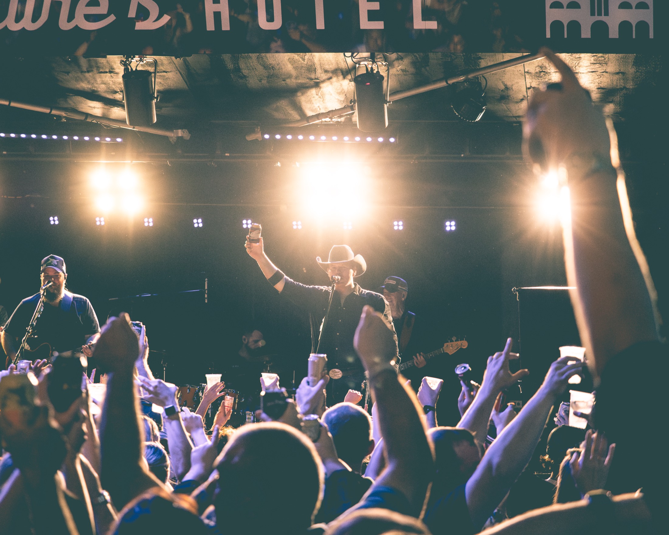 Packed crowd with hands and drinks raised at a hotel show