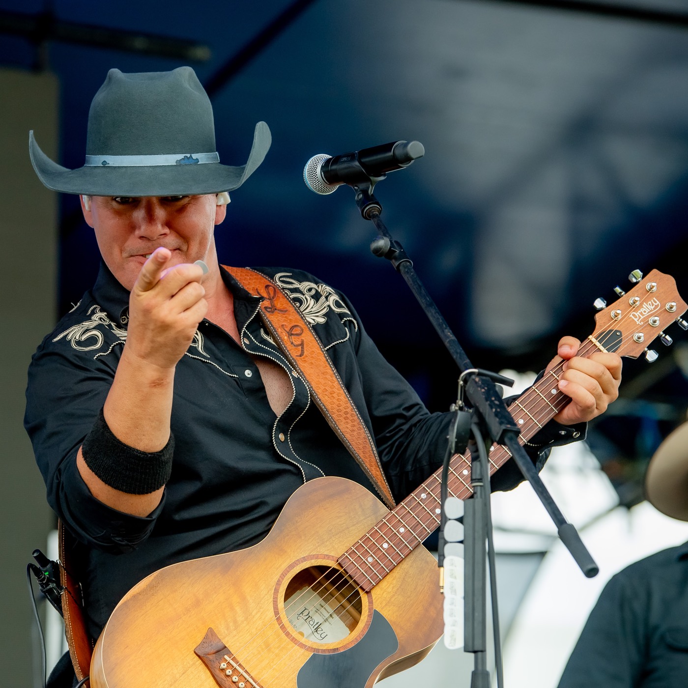 Luke Geiger in a grey cowboy hat playing an acoustic guitar