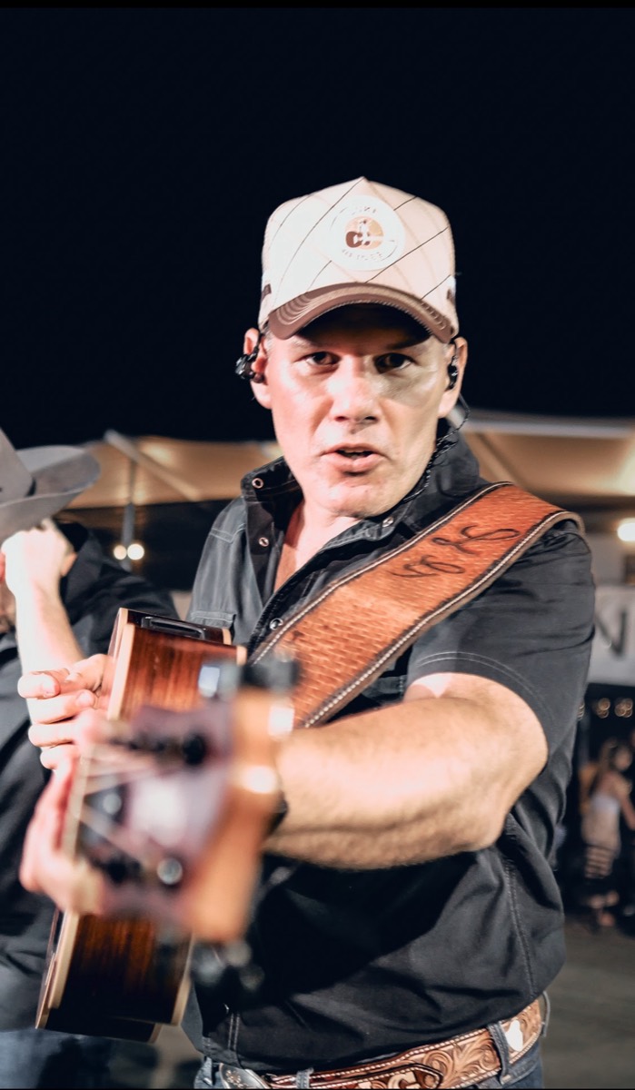 Luke Geiger playing at night in a cap and tooled leather guitar strap